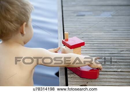 Rear view of male toddler playing with toy boat on pier View Large Photo Image Stock Photo - Rear view of male toddler playing with toy boat on pier. Fotosearch