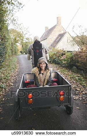 Stock Image - Rear view of mature hippy couple riding tricycle and trailer on rural road. Fotosearch