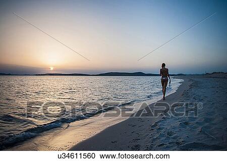 "Rear view of young woman strolling on beach carrying bikini top, Cagliari, Sardinia, Italy" View Large Photo Image Stock Image - "Rear view of young woman strolling on beach carrying bikini top, Cagliari, Sardinia, Italy". Fotosearch