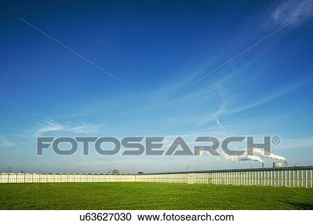 Stock Image - Rows of greenhouses in front of distant power station. Fotosearch