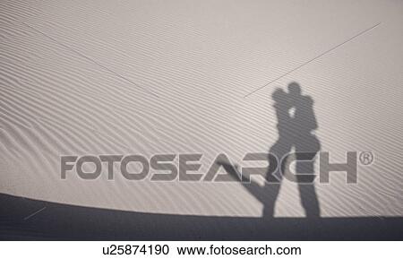 Stock Image - "Sand shadow of cute couple embracing, Cagliari, Sardinia, Italy". Fotosearch