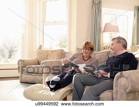 "Senior couple at home on sofa, looking at digital tablets" View Large Photo Image Stock Image - "Senior couple at home on sofa, looking at digital tablets". Fotosearch