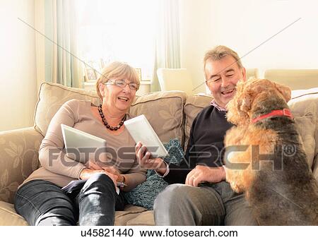 Stock Image - "Senior couple at home with dog, using digital tablets". Fotosearch