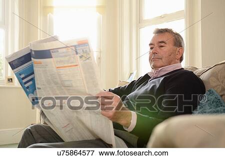 Stock Photo - Senior man sitting in armchair reading newspaper. Fotosearch