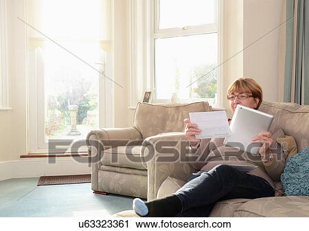 Senior woman sitting on sofa using digital tablet View Large Photo Image Stock Image - Senior woman sitting on sofa using digital tablet. Fotosearch