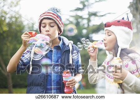Stock Photo - Siblings blowing bubbles in garden. Fotosearch