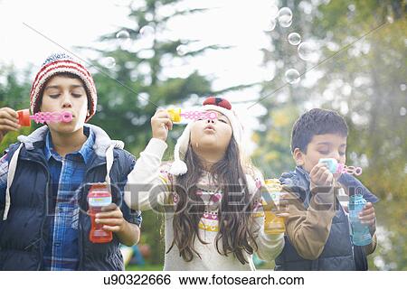Stock Photograph - Siblings blowing bubbles in garden. Fotosearch