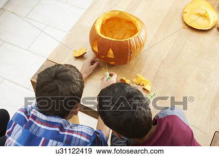 Siblings carving pumpkin in dining room View Large Photo Image Stock Photo - Siblings carving pumpkin in dining room. Fotosearch