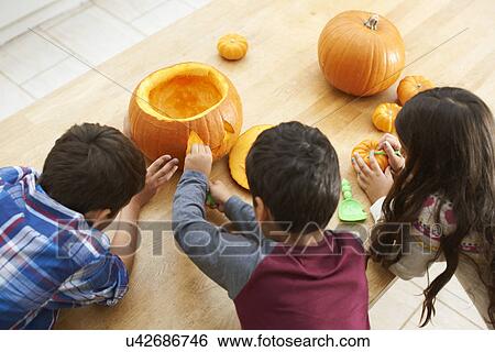 Siblings carving pumpkin in dining room View Large Photo Image Stock Photograph - Siblings carving pumpkin in dining room. Fotosearch