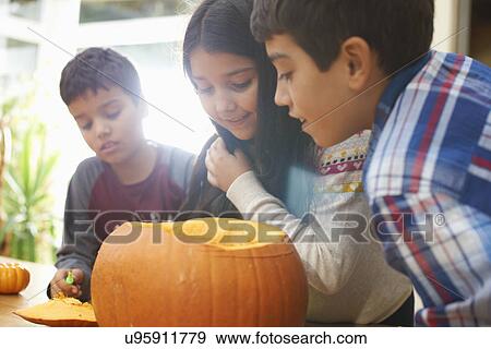Stock Photo - Siblings hollowing out pumpkin in dining room. Fotosearch