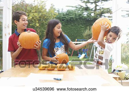 Stock Photograph - Siblings playing with pumpkin in dining room. Fotosearch