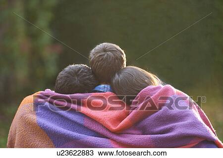 Stock Image - Siblings wrapped in blanket in garden. Fotosearch