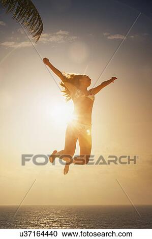 Stock Image - "Silhouette of young woman jumping mid air in sunset over sea, Etosha National Park, Namibia". Fotosearch