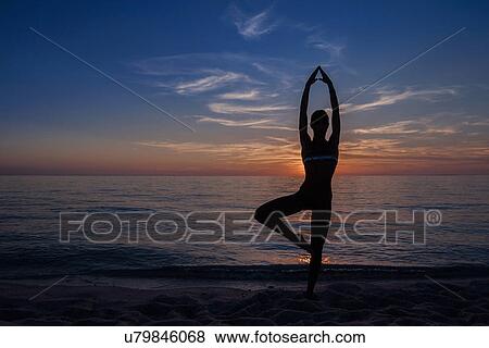Stock Photo - "Silhouetted young woman in yoga pose on beach at sunset, Oristano, Sardinia, Italy". Fotosearch