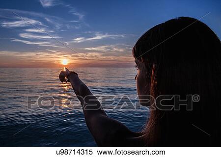 Stock Photography - "Silhouetted young woman pointing at sunset from beach, Oristano, Sardinia, Italy". Fotosearch