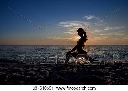 Stock Image - "Silhouetted young woman practicing yoga at sunset, Oristano, Sardinia, Italy". Fotosearch