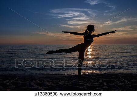 "Silhouetted young woman practicing yoga pose on beach at sunset, Oristano, Sardinia, Italy" View Large Photo Image Stock Photo - "Silhouetted young woman practicing yoga pose on beach at sunset, Oristano, Sardinia, Italy". Fotosearch