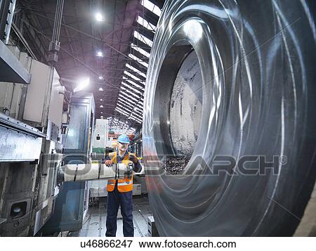 Stock Photo - Steelworker inspecting cutting tool in engineering factory. Fotosearch