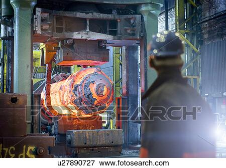 Stock Photo - Steelworker inspects hot steel in forging press in steelworks. Fotosearch