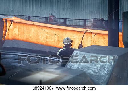 Stock Photo - Steelworker measures red hot steel in forging press in steelworks. Fotosearch