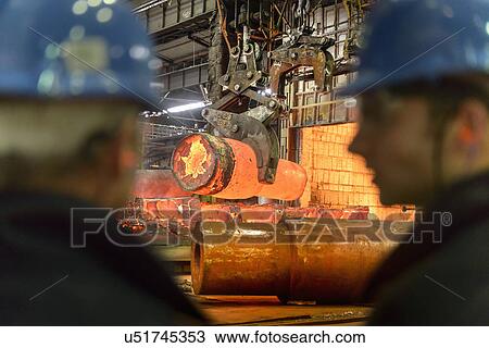 Stock Image - Steelworkers in front of hot steel casting on crane in steelworks. Fotosearch