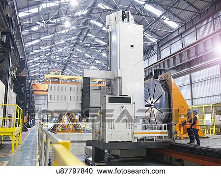 Stock Image - Steelworkers with gantry milling machine in engineering factory. Fotosearch