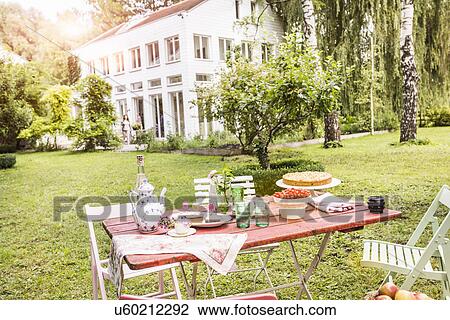 Stock Image - "Table in garden with teapot, tea cups, cakes and refreshments". Fotosearch