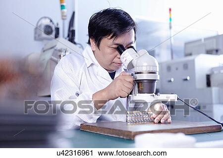 Stock Image - Technician using microscope in LED factory. Fotosearch