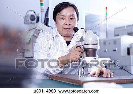 Stock Image - Technician with microscope in LED factory. Fotosearch