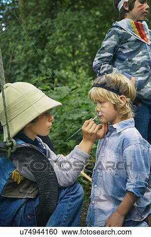 Stock Image - Three boys playing dress up in forest with face paint. Fotosearch