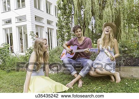 "Three friends in garden, man playing guitar" View Large Photo Image Stock Image - "Three friends in garden, man playing guitar". Fotosearch