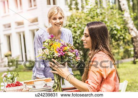 Stock Image - "Two female friends in garden, looking at bunch of flowers". Fotosearch