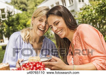 "Two female friends in garden, laughing, holding plate with dessert" View Large Photo Image Stock Image - "Two female friends in garden, laughing, holding plate with dessert". Fotosearch