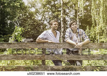 Two male adult friends leaning against garden fence View Large Photo Image Stock Image - Two male adult friends leaning against garden fence. Fotosearch