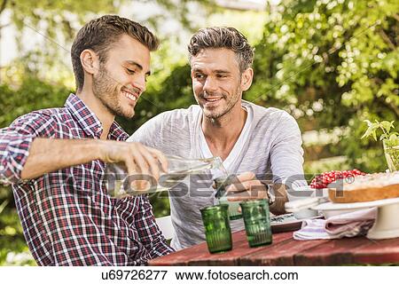 Stock Photo - Two male friends having drink together at table in garden. Fotosearch