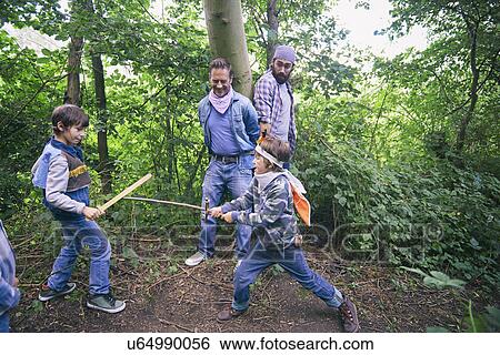Stock Photograph - Two men captured whilst boys have sword fight in forest. Fotosearch