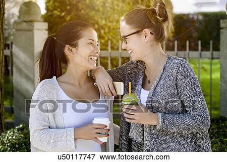 Two young female friends in park laughing and drinking takeaway coffee View Large Photo Image Stock Photo - Two young female friends in park laughing and drinking takeaway coffee. Fotosearch