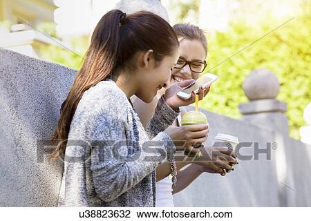 Two young women leaning against park wall laughing and drinking takeaway coffee View Large Photo Image Stock Image - Two young women leaning against park wall laughing and drinking takeaway coffee. Fotosearch