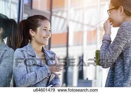 Stock Photo - Two young women with takeaway coffee laughing. Fotosearch