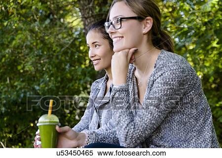 Two young women with takeaway coffee sitting in park View Large Photo Image Stock Photography - Two young women with takeaway coffee sitting in park. Fotosearch