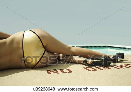 Stock Photo - Waist down of young woman wearing gold bikini bottoms lying poolside. Fotosearch