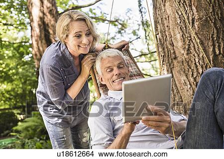 Wife watching husband using digital tablet on hammock View Large Photo Image Picture - Wife watching husband using digital tablet on hammock. Fotosearch