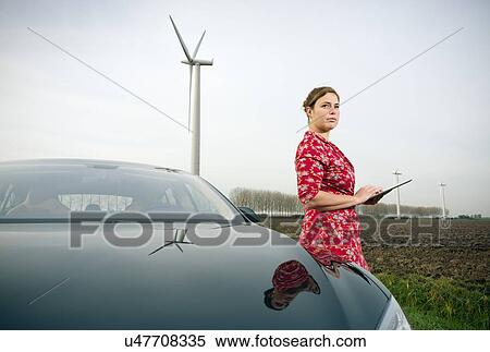 Stock Photography - Woman by car with wind turbine in background. Fotosearch