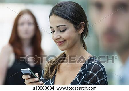 "Woman using phone, colleagues beside her" View Large Photo Image Picture - "Woman using phone, colleagues beside her". Fotosearch