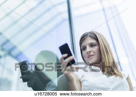 Stock Photography - Woman using smartphone against glass window. Fotosearch