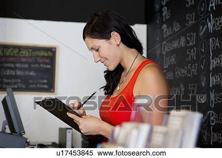 Stock Photography - Woman writing on clipboard in shop. Fotosearch