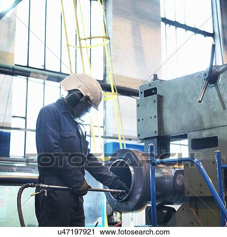 Stock Image - Worker polishing inside of tube in engineering factory. Fotosearch