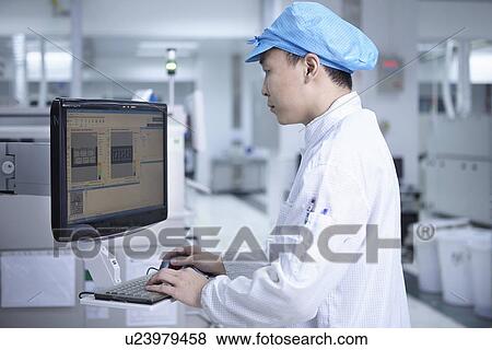 Stock Photo - Worker using computer in factory that specialises in creating functional circuits on flexible surfaces. Fotosearch