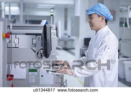 Stock Photo - Worker using computer in factory that specialises in creating functional circuits on flexible surfaces. Fotosearch