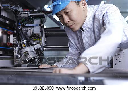Stock Image - Worker using machinery in factory that specialises in creating functional circuits on flexible surfaces. Fotosearch